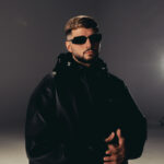 white man named dardan with black sunglasses and a black jacket in front of a dark background