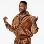 Black man named YG with a brown top and body jewelry in front of a white background